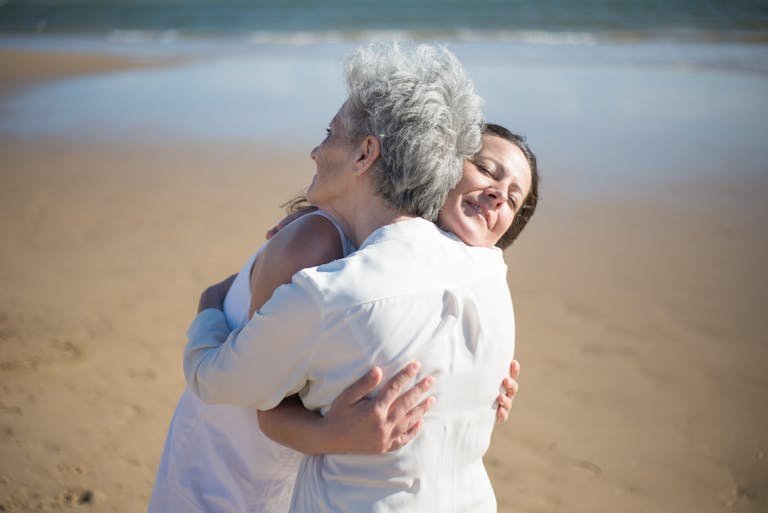 Mother and daughter share a heartfelt embrace on a sunny beach, expressing love and warmth.